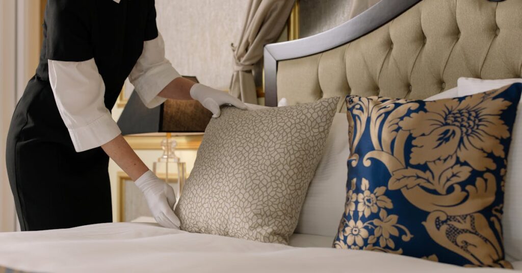 A chambermaid arranges pillows in a luxurious hotel room, showcasing comfort and elegance.
